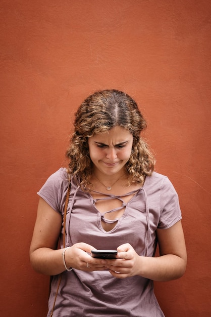 Jonge vrouw met mobiele telefoon terwijl ze tegen de muur staat