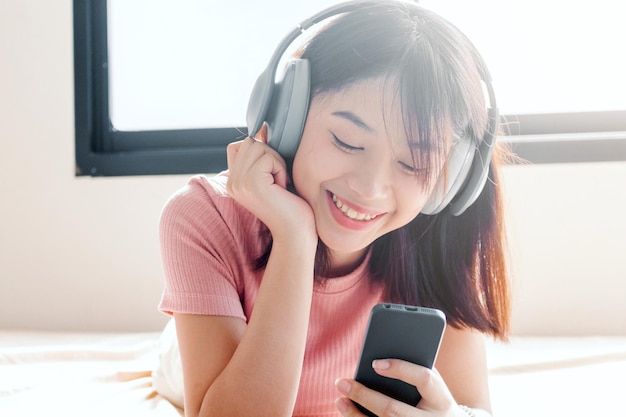 Jonge vrouw met mobiele telefoon terwijl ze thuis op bed ligt
