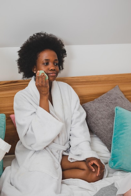 Jonge vrouw met mobiele telefoon terwijl ze thuis op bed ligt