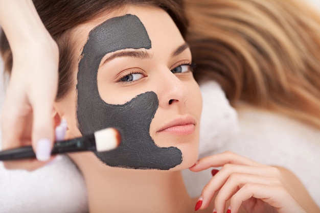 Jonge vrouw met natuurlijk gezichtsmasker in beauty spa