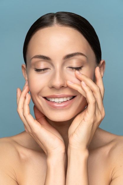 Jonge vrouw met natuurlijke make-up, gekamd haar, haar goed verzorgde pure huid op gezicht aan te raken