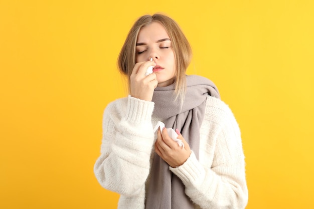 Jonge vrouw met neusdruppels op gele achtergrond, loopneus concept