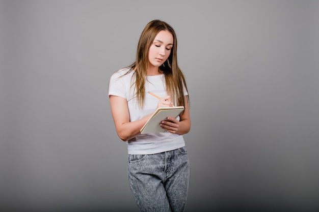 Jonge vrouw met notitieboekje en potlood die op grijze achtergrond schrijven