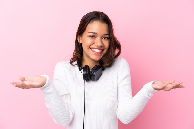 Jonge vrouw met oortelefoons over roze muur met geschokte gelaatsuitdrukking