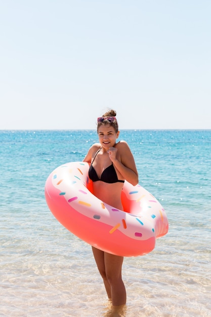 Jonge vrouw met opblaasbare ring koude rillingen triest gekruiste armen zwarte bikini zwembroek staande in zeewater. Zomervakantie en vakantie concept.