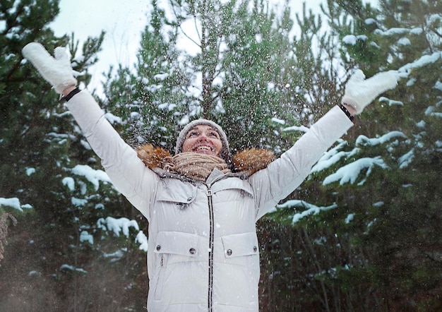 Jonge vrouw met opgeheven handen in het winterwoud Vrouw die sneeuw gooit met haar handen