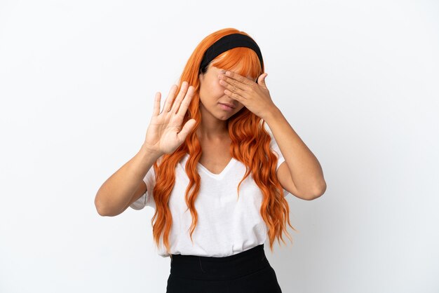 Jonge vrouw met oranje haar geïsoleerd op een witte achtergrond die stopgebaar maakt en gezicht bedekt
