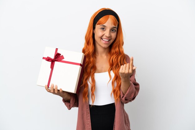 Jonge vrouw met oranje haar met een geschenk geïsoleerd op een witte achtergrond die komend gebaar doet