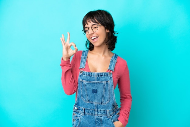 Jonge vrouw met overall geïsoleerde achtergrond die ok teken met vingers toont