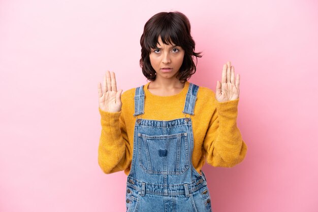 Jonge vrouw met overall geïsoleerde achtergrond die stopgebaar maakt en teleurgesteld is?