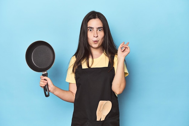Jonge vrouw met pan op blauwe studio met een geweldig idee concept van creativiteit