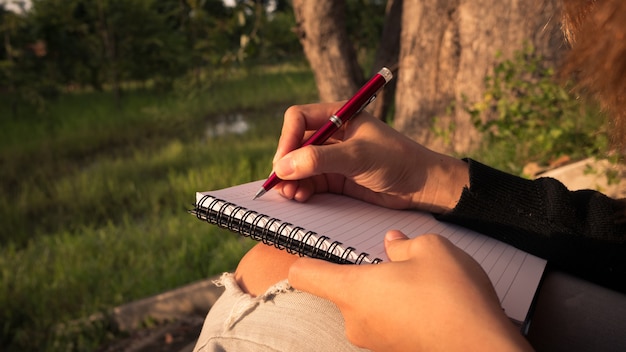 Jonge vrouw met pen die op notitieboekje bij aard schrijft.