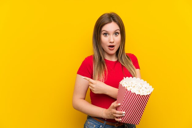 Jonge vrouw met popcorns over roze muur verrast en wijzende kant