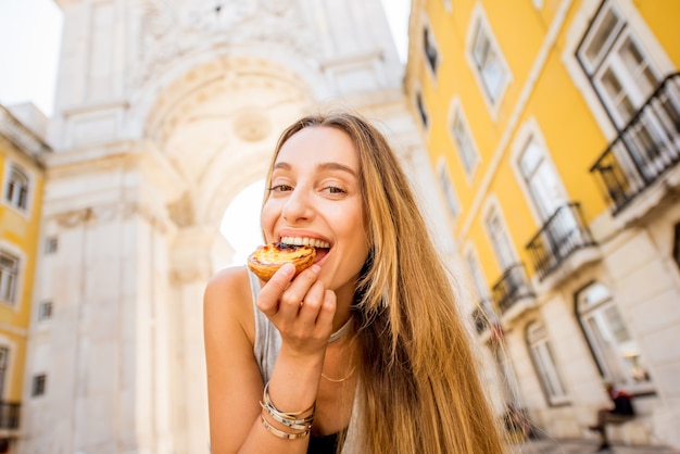 Jonge vrouw met Portugees eiertaartgebak genaamd pastel de Nata buiten op de triomfboogachtergrond in Lissabon