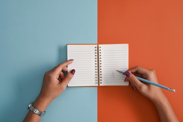 Jonge vrouw met potlood schrijven op lege notebook Top view