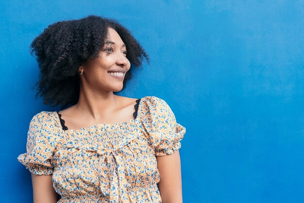 Jonge vrouw met prachtig afrohaar Ze kijkt naar de camera met een lachende uitdrukking tegen een blauwe achtergrond