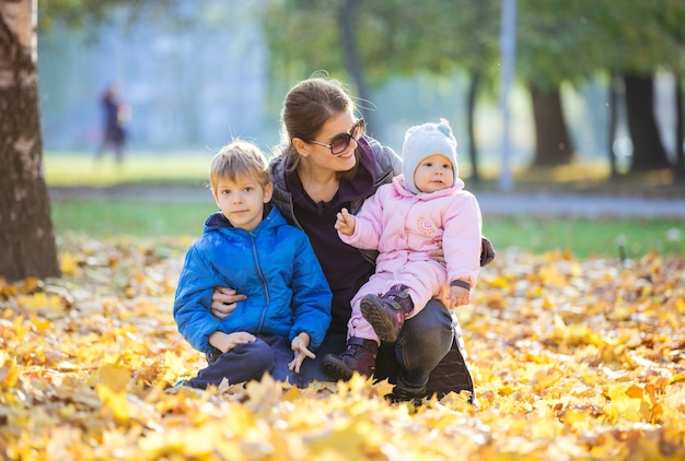 Jonge vrouw met preschool zoon en baby dochter genieten van mooie dag in herfst park