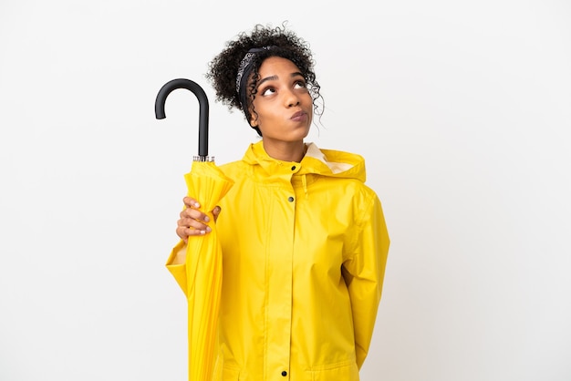 Jonge vrouw met regendichte jas en paraplu geïsoleerd op een witte achtergrond en opzoeken