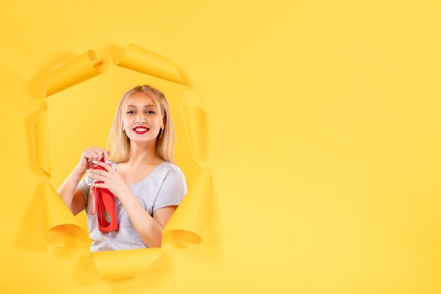 Jonge vrouw met rode fles op gele muur
