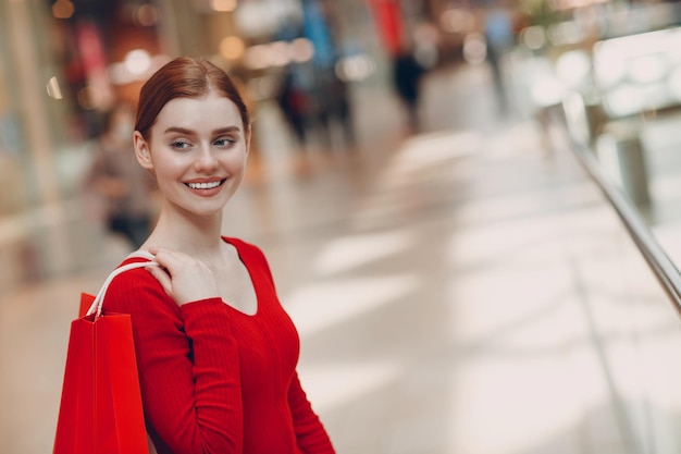 Jonge vrouw met rode papieren zakken in winkelcentrum Black friday en Valentijnsdag concept