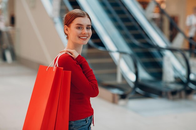 Jonge vrouw met rode papieren zakken in winkelcentrum Black friday en Valentijnsdag concept