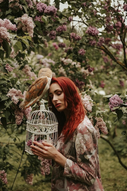 Jonge vrouw met rood haar in een lila tuin met een uil kerkuil