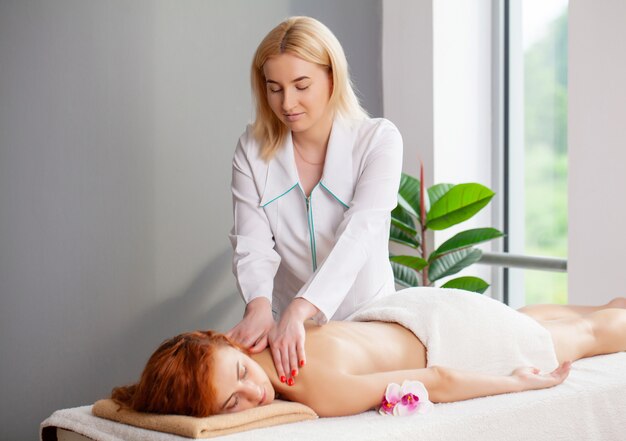 Jonge vrouw met rood haar krijgt een therapeutische rugmassage