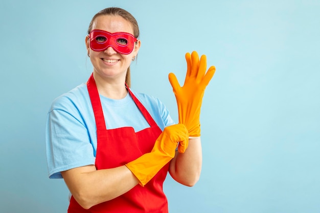 Jonge vrouw met rood oogmasker en schort draagt rubberen handschoenen op blauwe achtergrond