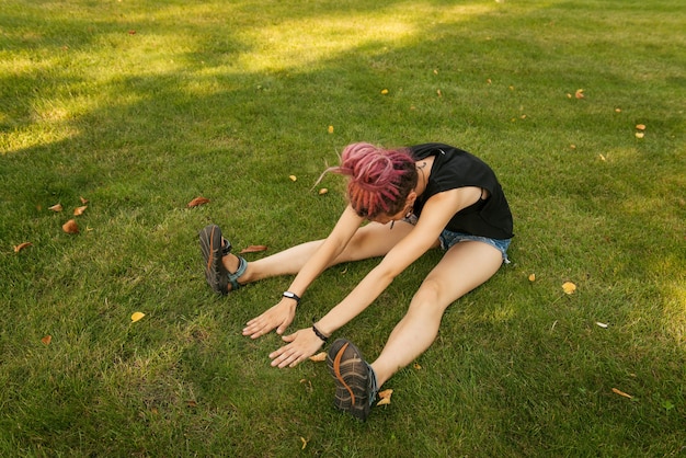 Jonge vrouw met roze dreadlocks doet yoga-oefeningen buiten in het park bij zonsondergang. Hard werk van beginner.