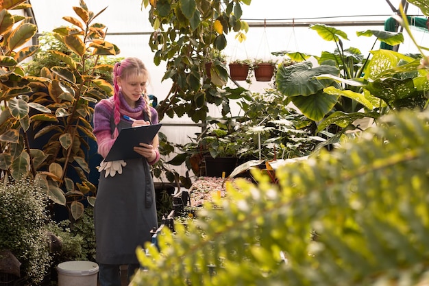 Jonge vrouw met roze haar die in serre van tuincentrum werkt