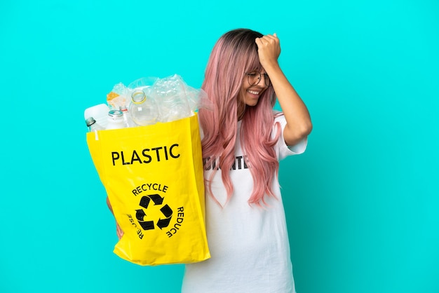 Jonge vrouw met roze haar met een zak vol plastic flessen om te recyclen, geïsoleerd op een blauwe achtergrond, heeft iets gerealiseerd en is van plan de oplossing te vinden