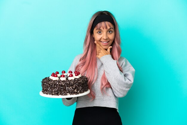 Jonge vrouw met roze haar met verjaardagstaart geïsoleerd op blauwe achtergrond gelukkig en glimlachend