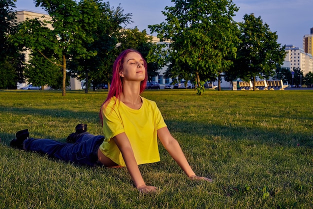 Jonge vrouw met roze haar traint yoga in stadspark in cobra pose