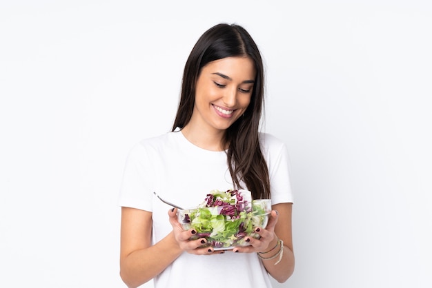 Jonge vrouw met salade die op witte muur wordt geïsoleerd