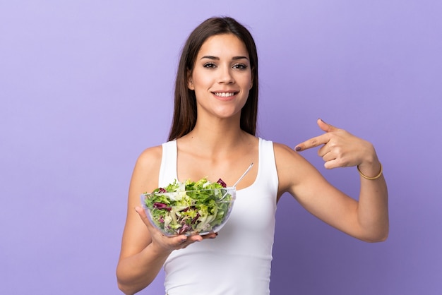 Jonge vrouw met salade geïsoleerd op paarse muur