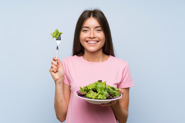 Jonge vrouw met salade over geïsoleerde blauwe muur