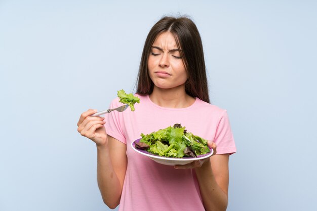 Jonge vrouw met salade over geïsoleerde blauwe muur