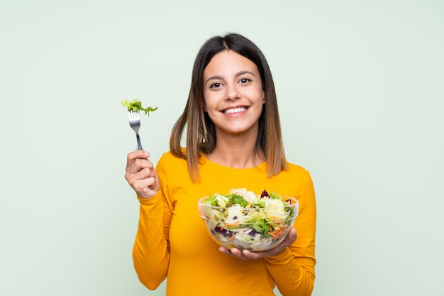 Jonge vrouw met salade over geïsoleerde groene muur