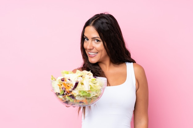 Jonge vrouw met salade over geïsoleerde muur