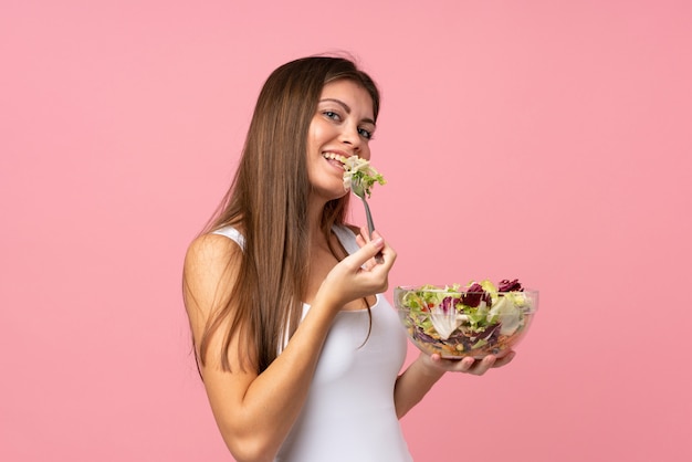 Jonge vrouw met salade over geïsoleerde roze muur