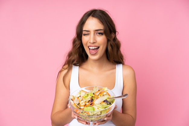 Jonge vrouw met salade over roze muur