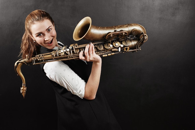 Jonge vrouw met saxofoon op zwarte achtergrond