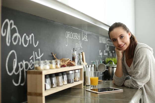 jonge vrouw met sinaasappelsap en tablet in de keuken