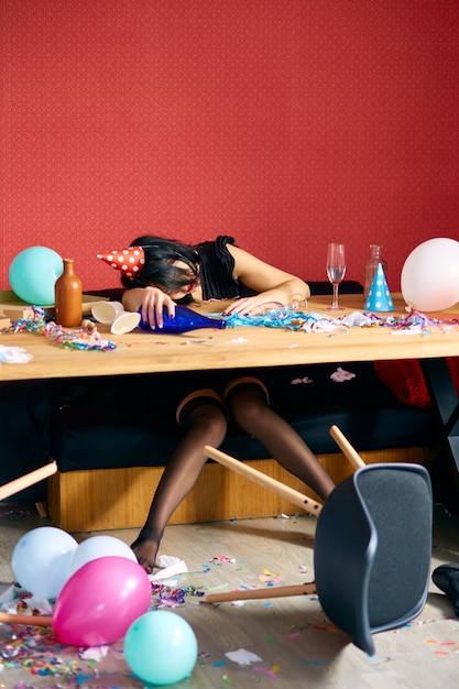 Jonge vrouw met slapen aan tafel in rommelige kamer na verjaardagsfeestje