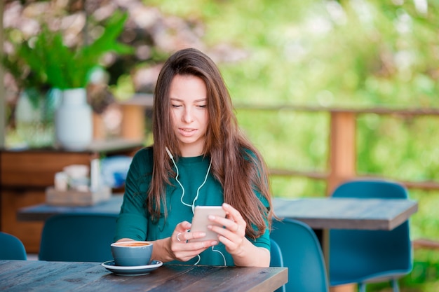Jonge vrouw met slimme telefoon terwijl het zitten alleen in koffiewinkel tijdens vrije tijd