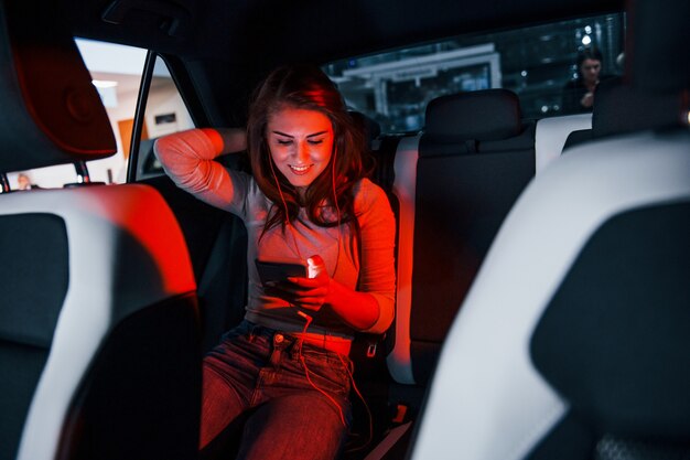 Jonge vrouw met smartphone is binnenkant van gloednieuwe moderne auto.