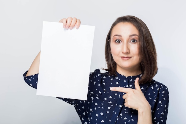 Jonge vrouw met teken business board, blanco, schoon wit papier op een witte achtergrond, kijkend naar hem