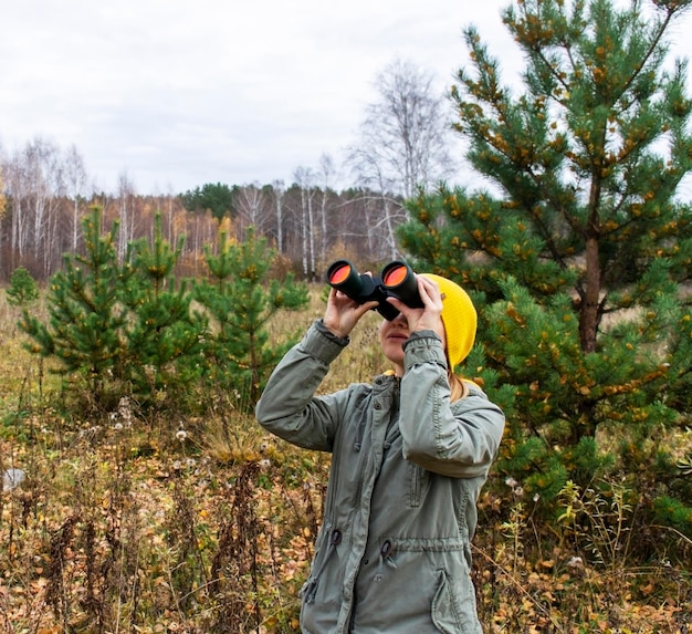 Jonge vrouw met verrekijker kijken naar vogels in het herfstbos Wetenschappelijk onderzoek