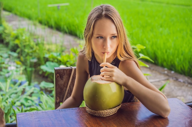 Jonge vrouw met verse kokoscocktail op de achtergrond van een rijstveld