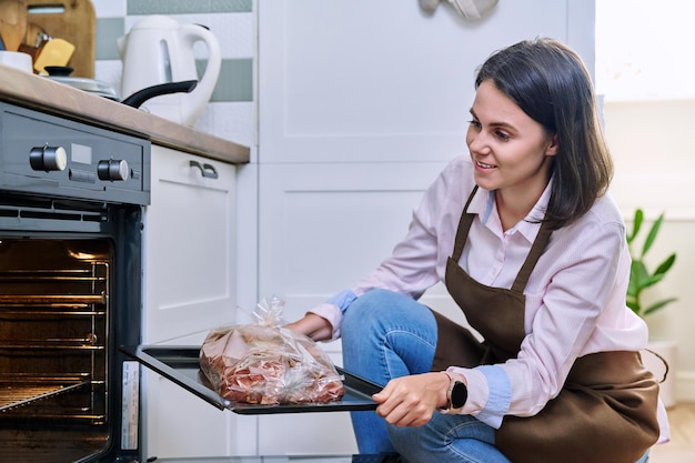 Jonge vrouw met vlees op bakplaat die ovenkeuken thuis opent